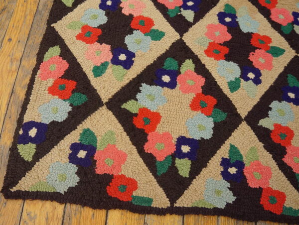 Hooked rug featuring colorful flowers in tan diamond lattices on a dark brown field, resting on wood planks.