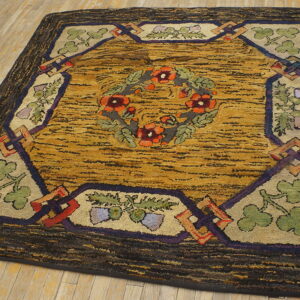 Textured rug featuring a central orange floral wreath, gold field, and dark patterned border on wood flooring.