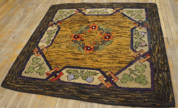 Textured rug featuring a central orange floral wreath, gold field, and dark patterned border on wood flooring.