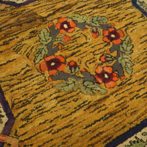 Highly textured, striped gold rug with a central floral wreath of red, orange, and green accents.