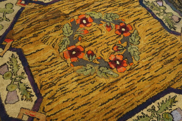 Highly textured, striped gold rug with a central floral wreath of red, orange, and green accents.