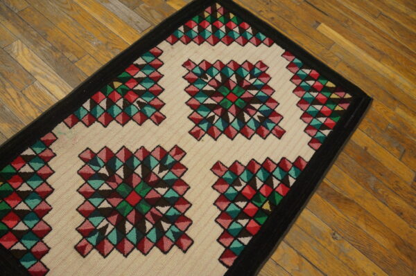 Runner rug with colorful geometric diamond designs and a black border rests on aged hardwood planks.