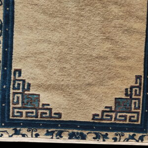 Tan field rug with an indigo border featuring floral scroll and geometric corner designs.
