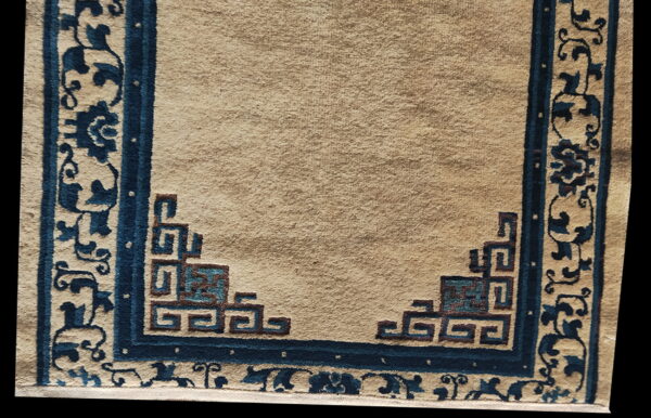 Tan field rug with an indigo border featuring floral scroll and geometric corner designs.