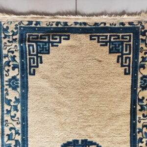 Beige rug with dark blue borders featuring geometric key patterns and scrolling florals on light gray tiles.
