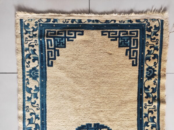 Beige rug with dark blue borders featuring geometric key patterns and scrolling florals on light gray tiles.