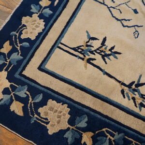 Beige rug with navy border and botanical motifs rests on distressed hardwood flooring.