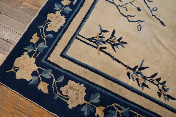 Beige rug with navy border and botanical motifs rests on distressed hardwood flooring.
