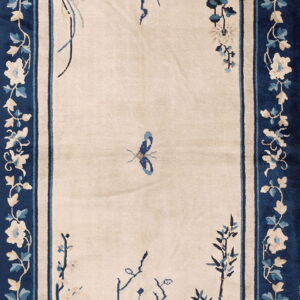 Cream rug featuring a central butterfly and blue floral branches, framed by a thick navy floral border.