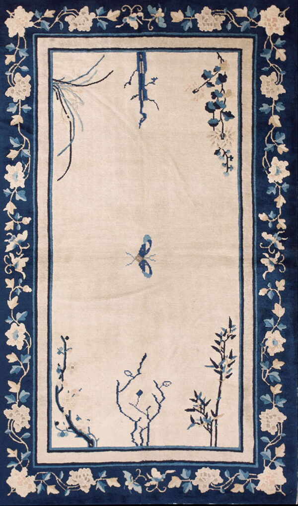 Cream rug featuring a central butterfly and blue floral branches, framed by a thick navy floral border.