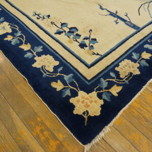 Cream rug with a wide navy blue floral border resting on distressed wood plank flooring.