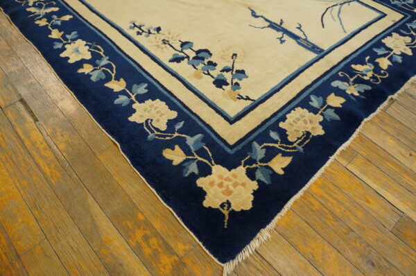 Cream rug with a wide navy blue floral border resting on distressed wood plank flooring.