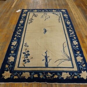 A cream field rug with a navy blue floral border and stylized bamboo motifs sits on wood floor planks.