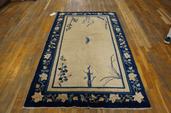 A cream field rug with a navy blue floral border and stylized bamboo motifs sits on wood floor planks.