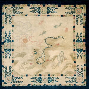 Pale square rug with faint blue and pink mythological figures and a prominent navy and cream scrolled border.