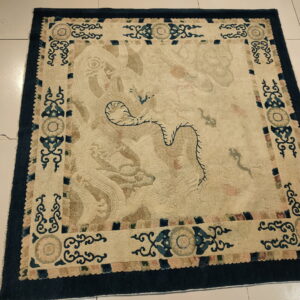 Intricate low pile rug with a cream field, navy border, and faded blue and tan mythological designs on white tile.