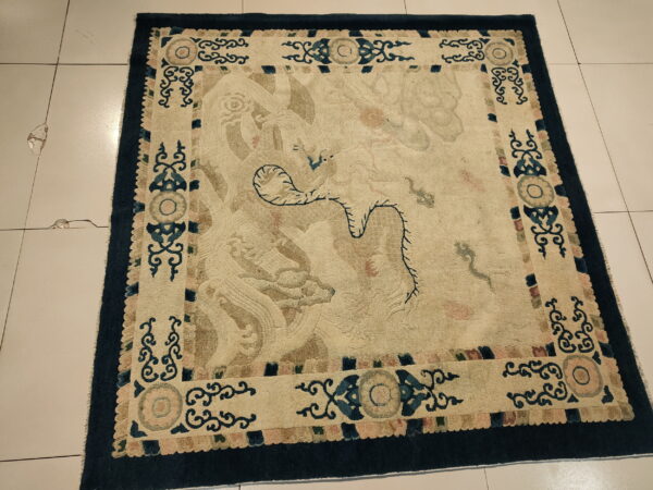 Intricate low pile rug with a cream field, navy border, and faded blue and tan mythological designs on white tile.