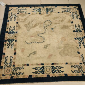 Cream rug with a central subtle dragon motif and a dark blue ornate border on light tile flooring.