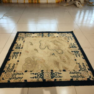 Faded square rug with abstract cream and blue patterns rests on glossy light beige tile.
