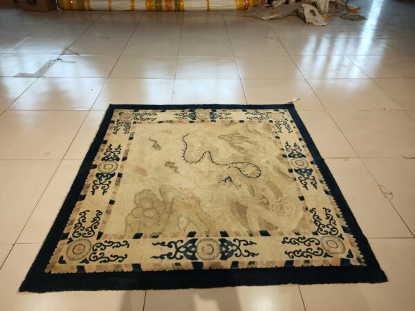 Faded square rug with abstract cream and blue patterns rests on glossy light beige tile.