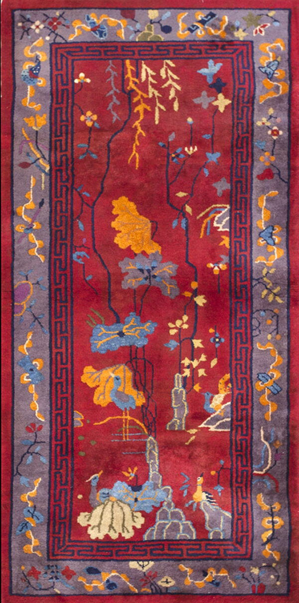 Rectangular rug with a red field featuring yellow and blue botanical scenes and bordered by a purple geometric trim.