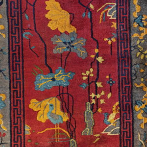 Deep red rug with stylized blue and yellow flowers, bird motifs, and a gray border with navy geometric lines.