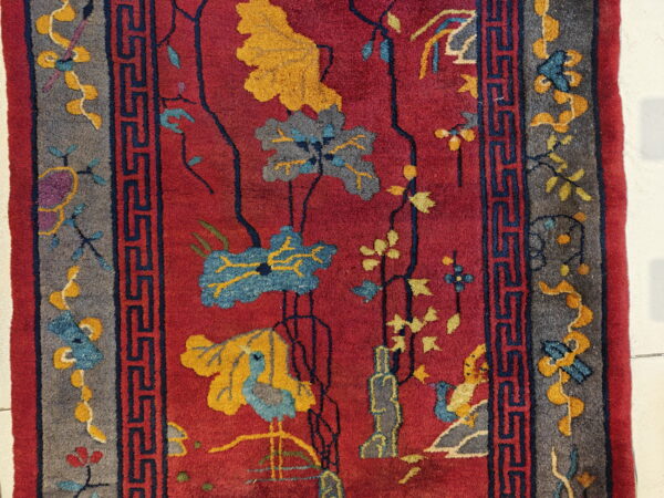 Deep red rug with stylized blue and yellow flowers, bird motifs, and a gray border with navy geometric lines.