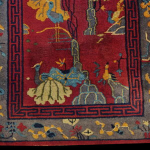 Vivid red rug with yellow and blue pictorial motifs, framed by a wide gray floral border and navy blue fret pattern.