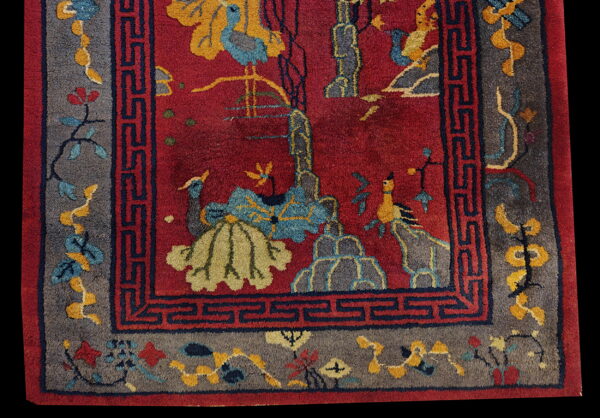 Vivid red rug with yellow and blue pictorial motifs, framed by a wide gray floral border and navy blue fret pattern.