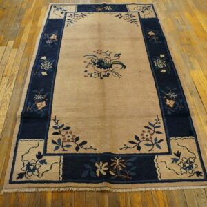 Tan area rug with a contrasting navy border and central floral spray on worn wood planks.