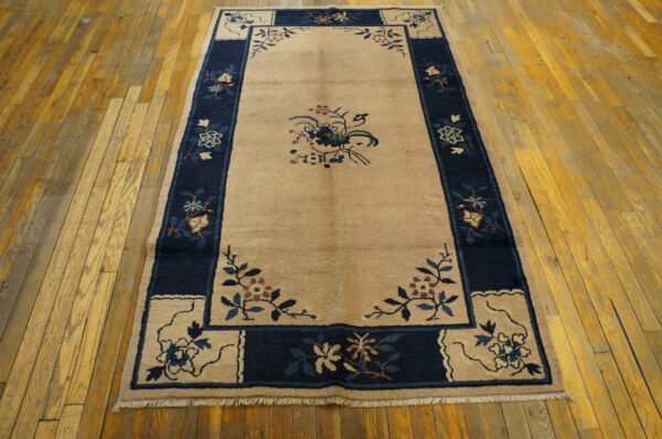 Tan area rug with a contrasting navy border and central floral spray on worn wood planks.