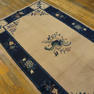 Low-pile beige rug featuring a navy blue floral border and motifs rests on rustic wood floors.