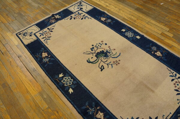 Low-pile beige rug featuring a navy blue floral border and motifs rests on rustic wood floors.