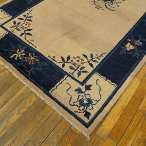Beige rug featuring a navy blue border with blue and brown floral patterns on aged wood floors.