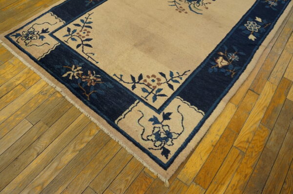 Beige rug featuring a navy blue border with blue and brown floral patterns on aged wood floors.