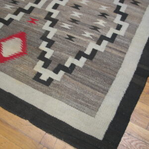 Gray flatweave rug featuring red diamond, black and white zigzag motifs, and striped borders on wood.