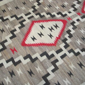 Flatweave rug in grey, black, and white features stepped geometric zig-zags and diamond shapes accented by red.