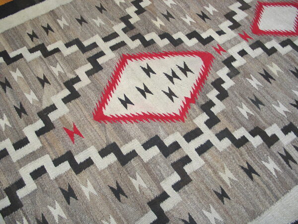 Flatweave rug in grey, black, and white features stepped geometric zig-zags and diamond shapes accented by red.