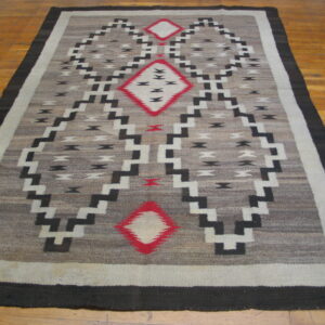 Gray and black geometric rug with red diamond accents lying on a warm-toned wood floor.