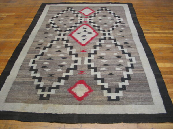 Gray and black geometric rug with red diamond accents lying on a warm-toned wood floor.