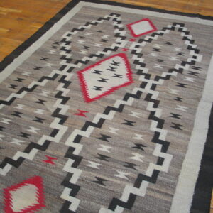 Gray flatweave rug featuring black and white zigzag patterns and three red-outlined diamonds on a wood floor.