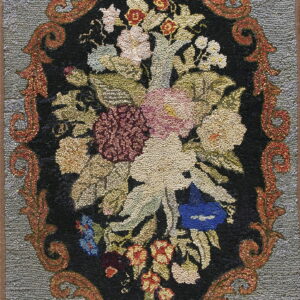 Textured loop pile rug featuring a detailed multicolored floral arrangement within an ornate reddish-orange oval border on a gray background.