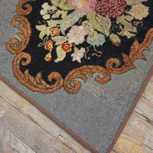 Low-pile gray rug with black floral pattern and rust scrollwork lies on rustic, weathered wooden flooring.