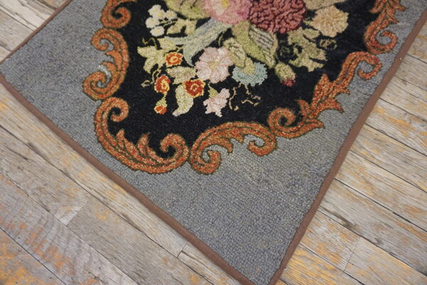 Low-pile gray rug with black floral pattern and rust scrollwork lies on rustic, weathered wooden flooring.