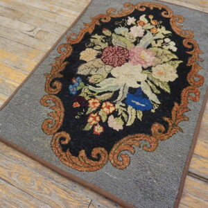 A gray rug featuring an ornate black floral medallion with orange scrolls rests on distressed wood planks.