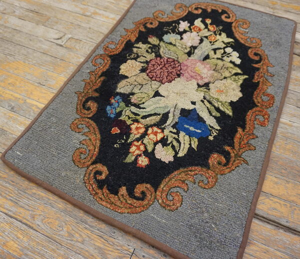 A gray rug featuring an ornate black floral medallion with orange scrolls rests on distressed wood planks.