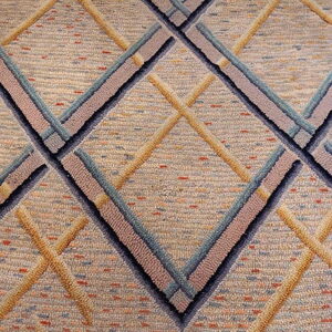 Raised diamond pattern rug in textured beige, gold, pale blue, and dark gray on wood floor.