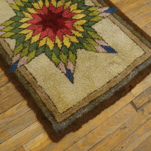 Close-up of a shaggy rug with a colorful starburst design and brown border on distressed wood floors.