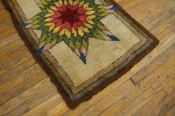 Close-up of a shaggy rug with a colorful starburst design and brown border on distressed wood floors.