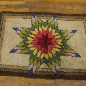 Textured rug with a multi-colored star design and thick brown border on plank wood floors.